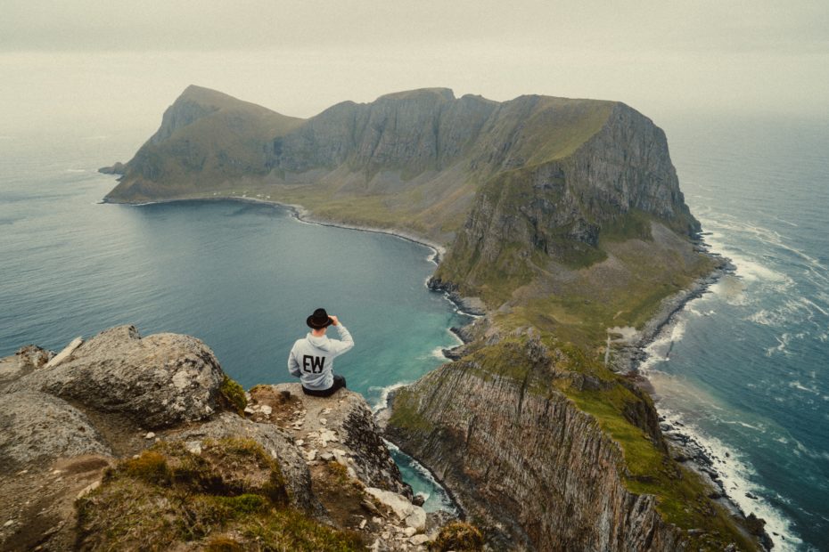 man in white shirt sitting on rock formation in front of body of water during daytime